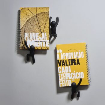 Bonequinhos escalando a parede "rumo à vaga em uma universidade". 2 Cadernos de estudos Planejamente apoiados neles.